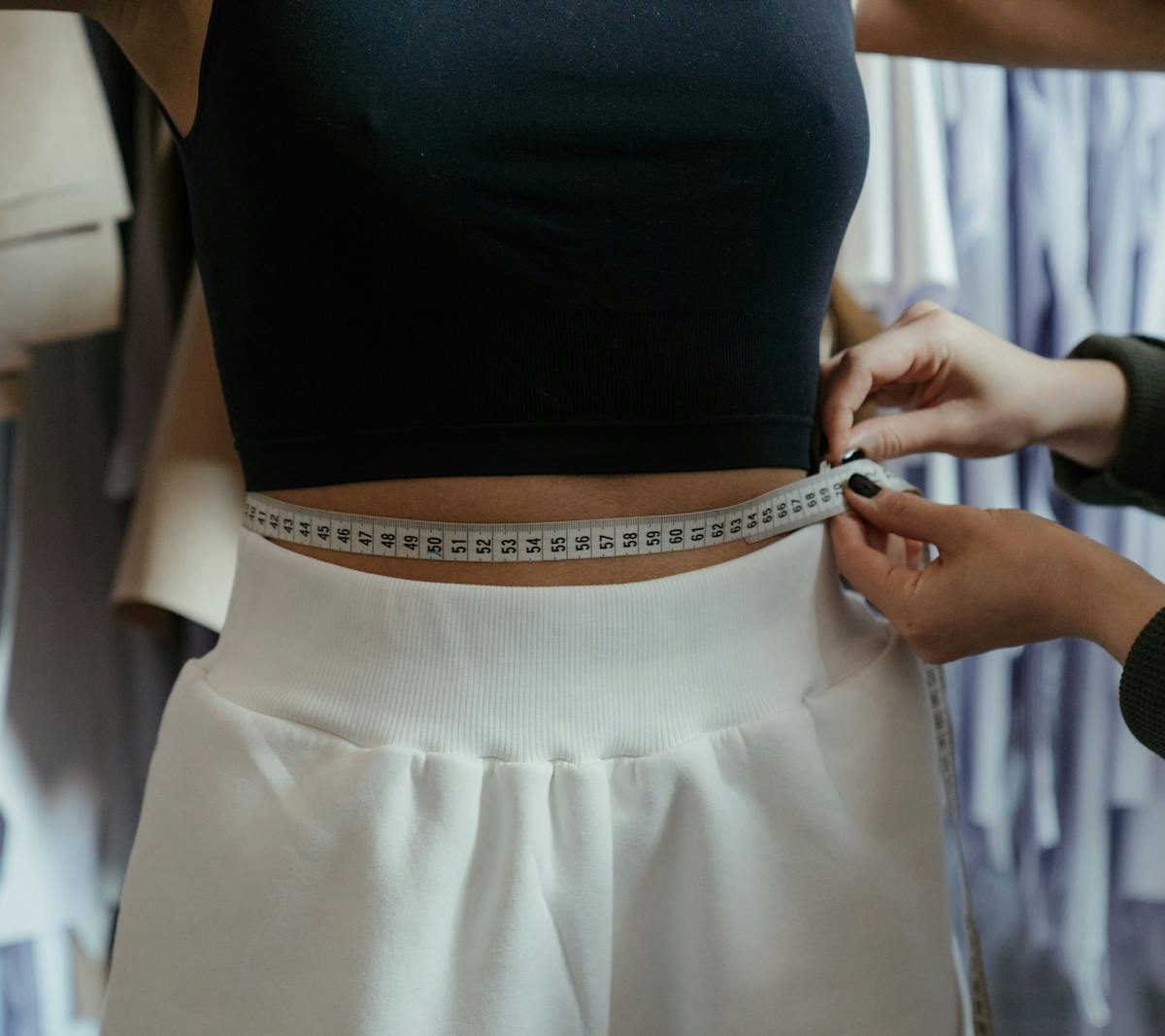 Costura Aranzazu Pamplona - Detailed view of a tailor measuring a client's waist in a clothing workshop, focusing on precision.